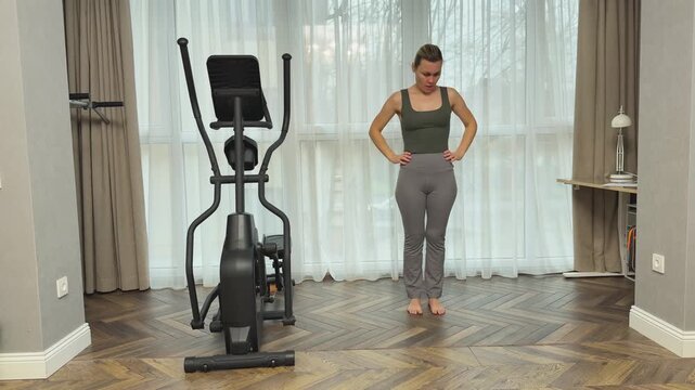 Woman bends forward trying to reach toes with both hands in living room. Home stretching routine improving flexibility, hamstring mobility and posture.