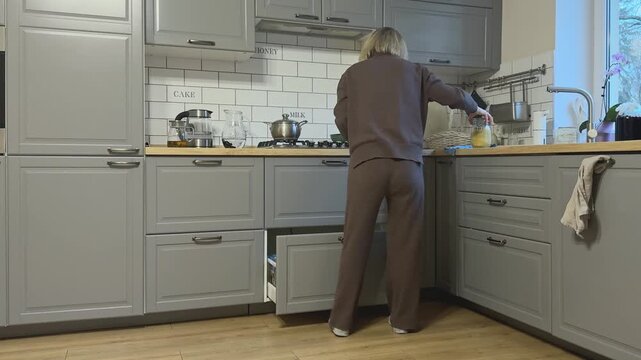 Female opens lower drawer, takes jar of rice and transparent bowl preparing to cook.