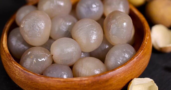 Longan kernels in a wooden container, peeled longan lies in a dense mass in a dish next to the remains of the shell and whole fruits.