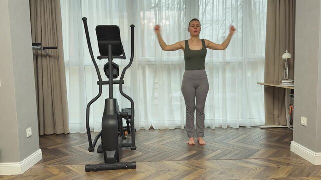 Woman performs arm rotations focusing on elbow joints and forearms in living room. Home warm up for mobility, injury prevention and preparation before workout.