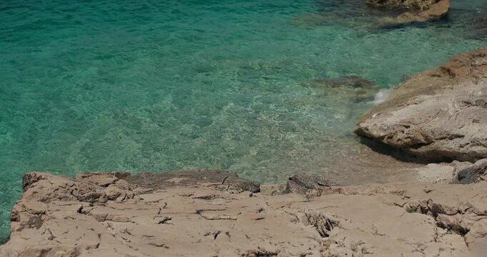 Crystal clear Adriatic water washes against rocky coastal formations in Primosten, Croatia.