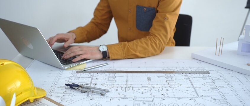 Architect working on new building development project, planning blueprints and collaborating on construction plans using a laptop and architectural models