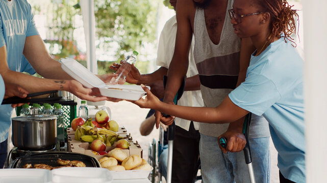 Voluntary individuals contributes to and offers humanitarian help to the underprivileged and needy, young black volunteer woman helps African American guy using crutches at a food drive.