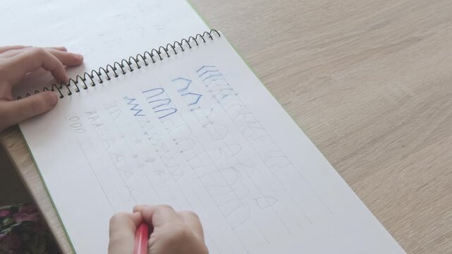 Close up preschool kid hand writing letter elements in notebook, practicing handwriting strokes, early literacy and school preparation concept, Developing fine motor skills and hand-eye coordination