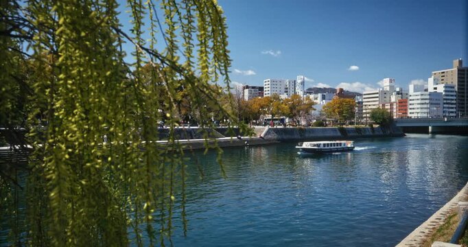 Willow Tree Framing Canal With Boat and City Skyline In Hiroshima Japan - Steady Cam
