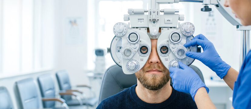 A person sits in an optometrist office while a specialist adjusts a vision testing device. The room has bright lighting. The test assesses eyesight clarity and focus