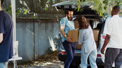 Less fortunate Caucasian woman and African American man are seen accepting donation box from male...
