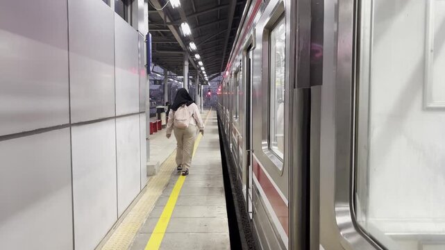 Female passengers wearing hijab rush to board a commuter train at a busy station platform, illustrating urban commuting and public transportation.