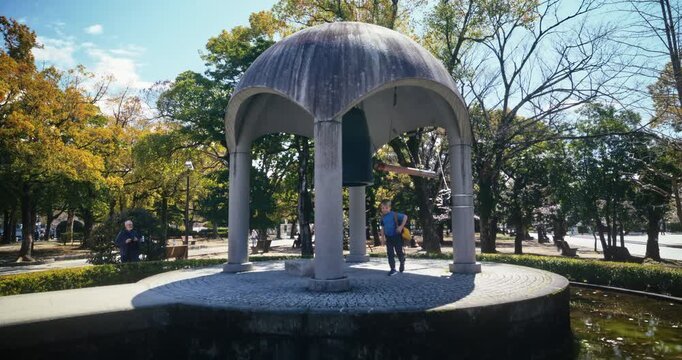Child Ringing Peace Bell Monument in Hiroshima Park - Wide, Tracking Shot