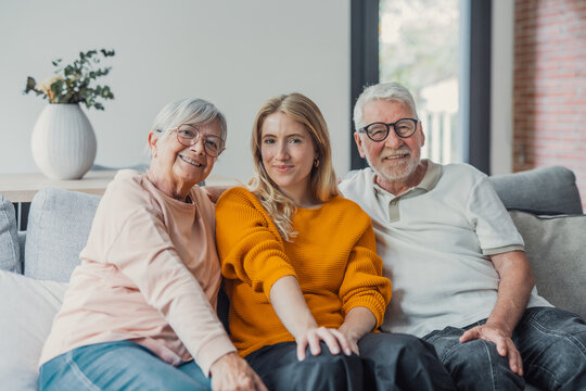 Happy family of different generations sitting on a gray sofa in a modern apartment, looking at the camera and sharing a warm, joyful moment of connection and togetherness