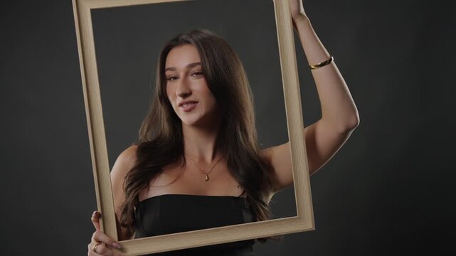 Beauty and self perception concept with a young woman posing in a studio, holding an empty picture frame. This image explores themes of identity, expression, and how individuals frame themselves for t