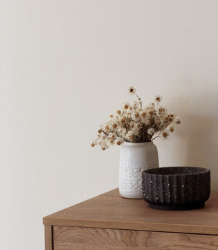 Modern interior still life of paper daisies in a vase next to a black terrazzo candle on a timber sideboard with copy space