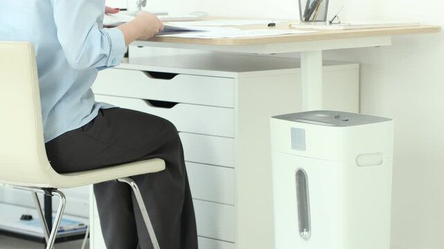 Woman destroying documents with paper shredder in office, closeup