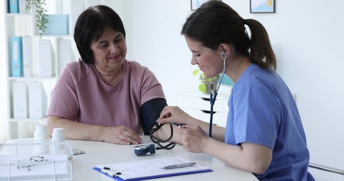 Nurse measuring woman's blood pressure with sphygmomanometer at table in hospital