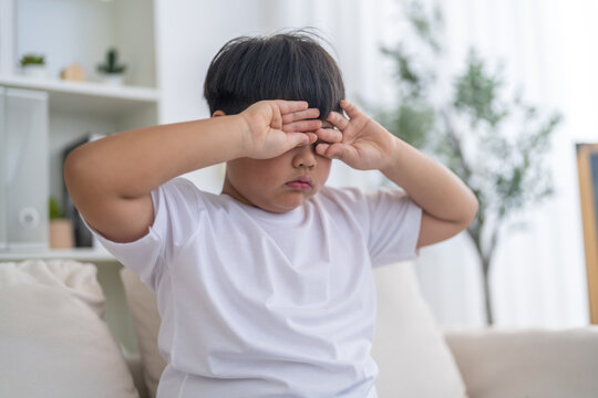 Asian boy rubbing his tired eyes from digital eye strain, vision problem, screen fatigue, childhood eye care, myopia prevention, physical discomfort, pediatric ophthalmology and medical health issue