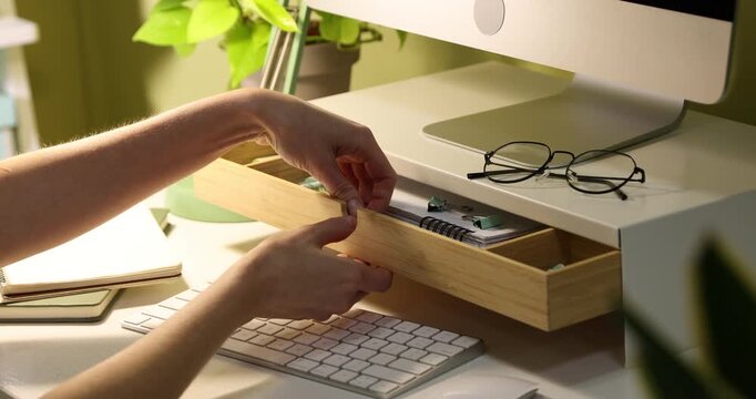 Woman taking highlighter from drawer of under monitor riser at desk indoors, closeup