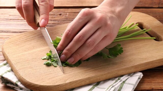 Woman cutting fresh parsley at wooden table, closeup