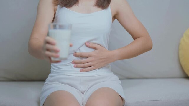 Lactose intolerance and Milk allergy concept. woman hold Milk glass and having abdominal cramps and pain when drink Cow Milk.Symptom stomach ache Dairy intolerant Nausea, Bloating Gas and Diarrhea.