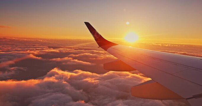 Airplane wing flying above sea of clouds at golden sunlight during sunset or sunrise in the sky cinematic video