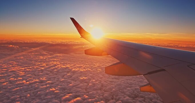 Scenic view from an airplane window showcasing the aircraft wing above a sea of fluffy cumulus clouds. Flying above clouds beautiful golden hour sunset 