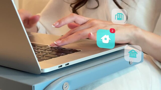 Close up of an East Asian woman using her laptop keyboard inside the house, with virtual building, house, park, and retail store architecture icons popping up.