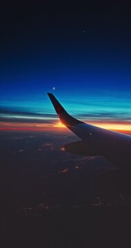 Airplane fly in sunset sky over earth of city light and wing of plane. View from the window of the Aircraft. Traveling in air.
