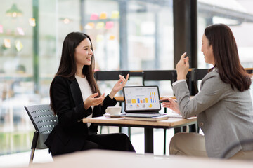 Fototapeta premium Businesswomen collaborating on a project, analyzing data charts on a tablet, discussing financial strategies and marketing plans during a corporate meeting in a modern office