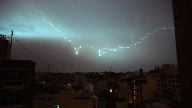 City skyline at dusk, viewed from a high vantage point. Buildings and power lines stretch across the urban landscape. Multiple bright lightning strikes illuminate the sky