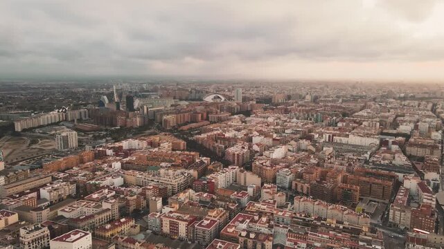 Aerial view of sprawling urban cityscape under cloudy sky. Buildings densely packed, red rooftops dominate the scene. Modern towers rise among traditional structures