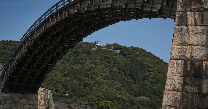 Wooden Arch Bridge Framing Ancient Castle on Forested Hill Of Japan - Low, locked off shot