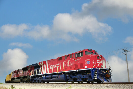Recently delivered, and specially painted to commemorate America's 250th birthday, a Kansas City Southern locomotive leads a CPKC freight train toward entry to a local rail yard. 