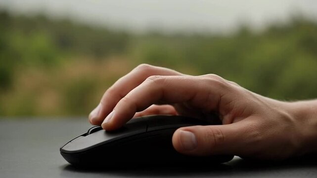 Hand using a computer mouse outdoors.