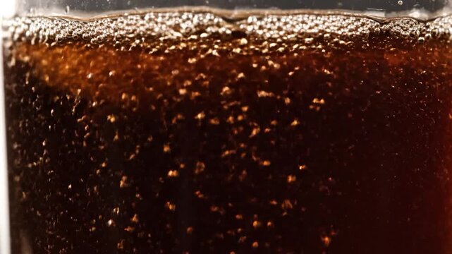 Close-up of effervescent bubbles rising in a dark carbonated beverage, creating a refreshing texture.