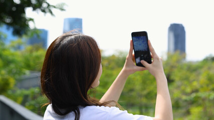Young Woman Using Smartphone to Capture City Skyline in Benchakitti Park © blueringmedia