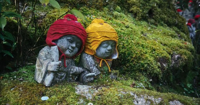 Two Stone Jizo Statues with Knit Hats on Mossy Slope Of Hiroshima, Japan - Closeup, Steady Cam