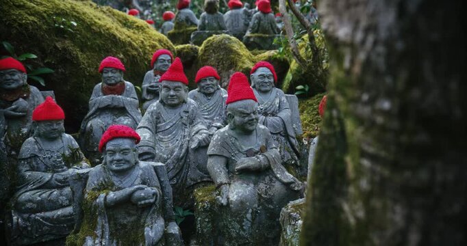 Small, Ancient Stone Rakan Statues with Red Knit Caps at Mossy Rock In Hiroshima, Japan - Slow Motion