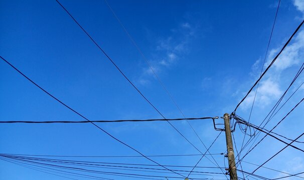 Clear blue sky with utility poles and intersecting power lines creating a geometric urban pattern. Minimalist outdoor scene featuring electrical infrastructure against a bright daytime sky.