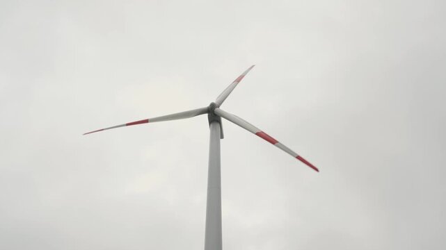 Single wind turbine with large blades spinning against an overcast sky, symbolizing clean renewable wind power, sustainable energy generation and environmental innovation