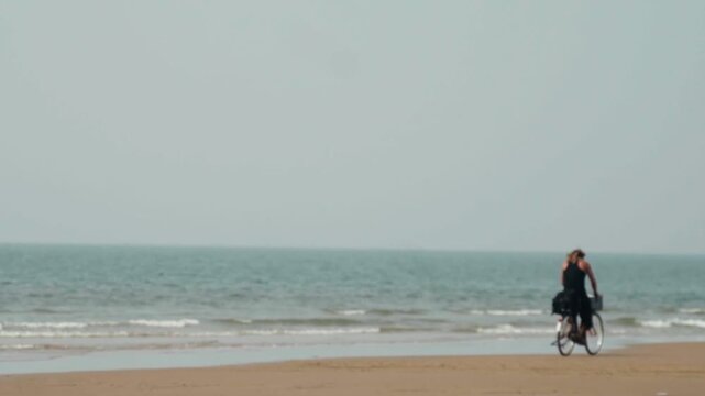 Beautiful woman with blonde hair riding a bicycle on a sandy beach during an overcast day, enjoying a peaceful and solitary moment by the sea with gentle waves in the background