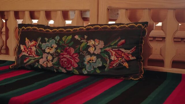Vintage wooden bench with a striped blanket and an embroidered floral pillow in a cozy, rustic interior. Handcrafted furniture and textile decorations creating a warm, nostalgic atmosphere