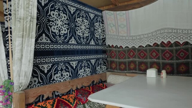 Authentic interior of a traditional Uzbek restaurant with ethnic patterns on carpets, embroidered pillows, and carved wooden furniture, creating a cozy and colorful national atmosphere