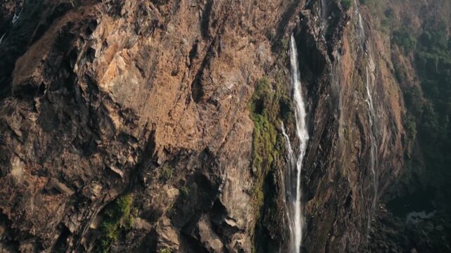 Majestic aerial perspective showing the stunning Jog Falls cascading down a rocky cliff surrounded by lush green mountains and forest, a popular tourist destination in Karnataka, India