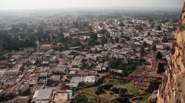 Panoramic view of the town of Badami in Karnataka, India, seen from a high vantage point, with its dense collection of buildings and surrounding hazy landscape revealing a typical rural settlement