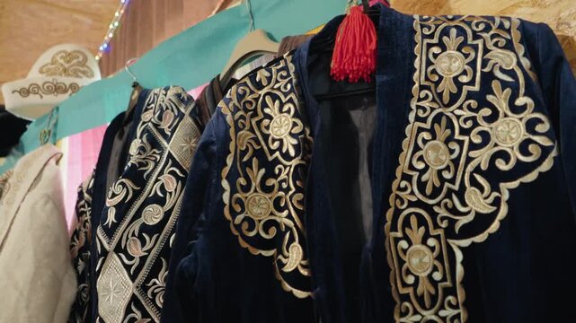 Authentic collection of traditional kazakh clothing with ornate gold embroidery hanging on display, showcasing the rich cultural heritage and craftsmanship of national costumes in a local market