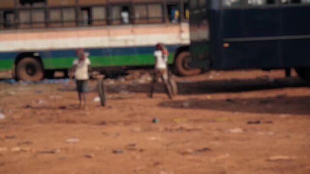 Unhappy childhood of two poor Indian boys playing with a tire in a dusty slum area next to an old, dirty bus, showing the reality of poverty and social issues in developing countries