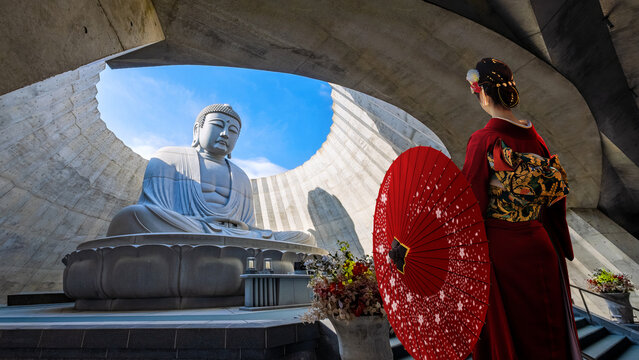 Young Japanese woman in a red traditional Kimono dress aith the big Buddha at Makomanai Takino Cemetery in Sapporo, Hokkaido, Japan