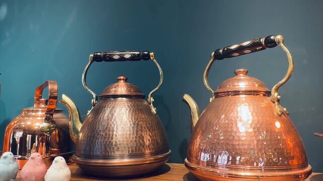 Traditional copper teapots with hammered texture and small ceramic bird figurines on wooden shelf. Authentic middle eastern kitchenware, vintage metallic kettles and rustic home decoration icons.