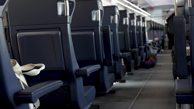 Empty passenger cabin interior inside modern commuter train showing rows of blue seats during travel.