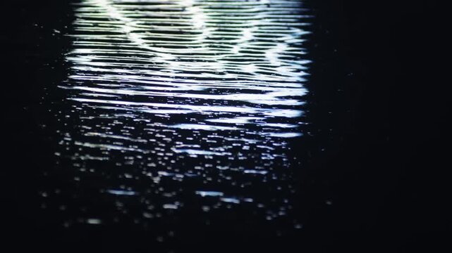 Glistening moonlight creating a mesmerizing reflection on the tranquil, dark surface of the water at night, with ripples and waves distorting the bright, abstract light pattern