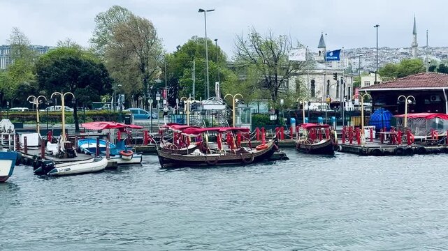 Traditional ottoman sultan boats with red canopies moored at pier in Eyup Sultan district, Istanbul. Maritime transport, public ferry station, historical mosque architecture and city embankment.